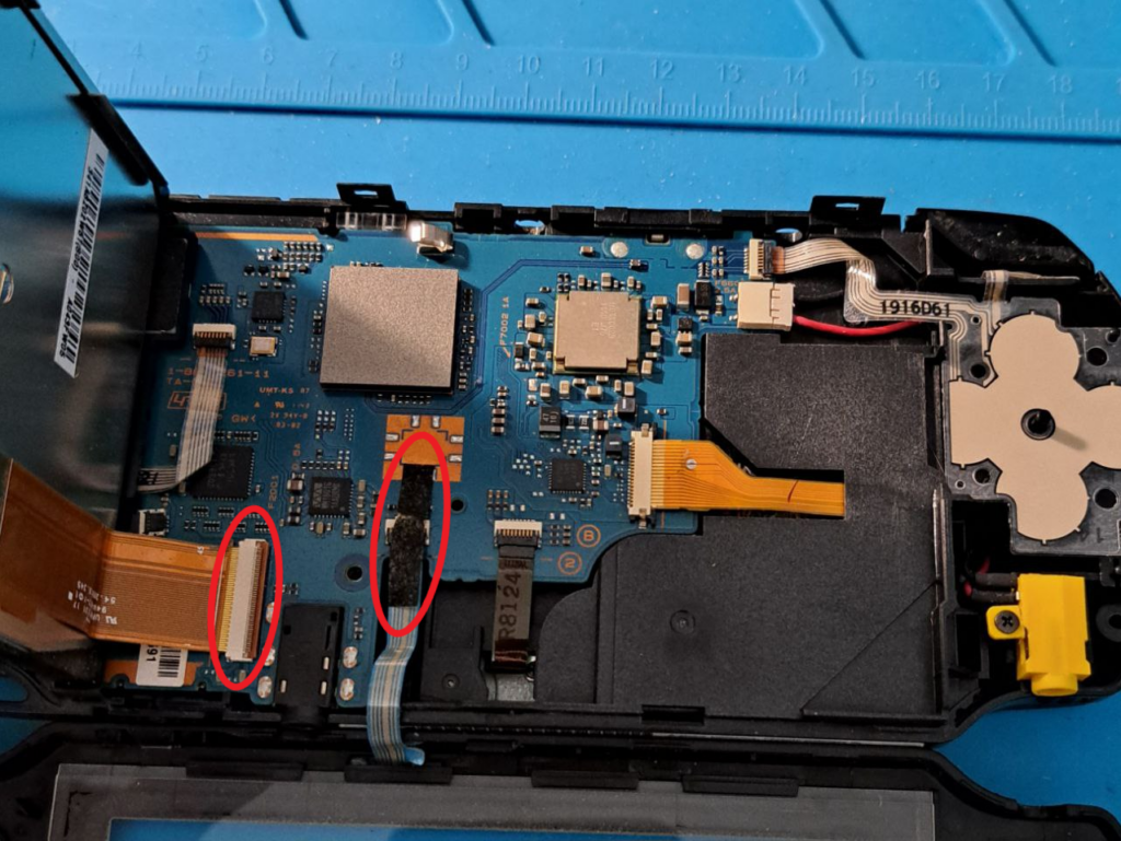 Nach links geklapptes Display. Das Motherboard ist vollständig zu sehen. Rot markiert sind die Flachbandkabel des Displays und der Bedienleiste unten.