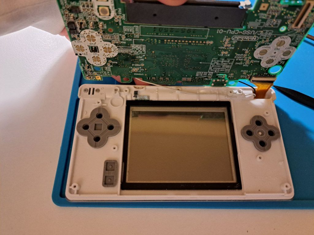 Touchscreen in weißem DS lite Gehäuse auf blauem Untergrund. Das Motherboard ist nach oben geklappt.